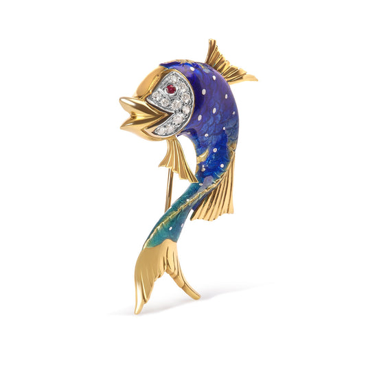 Yellow metal fish-shaped brooch with blue and green enamel and white and red gemstones on the face, shown from a front side angle.