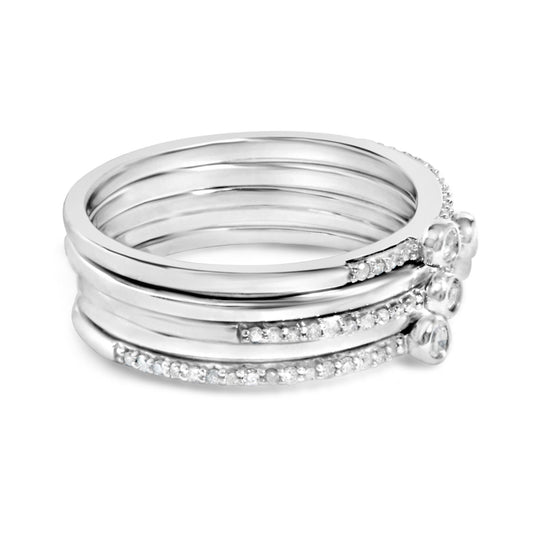 Stacked white metal rings with white round gemstones in bezel and prong settings, shown in a close-up side angle.