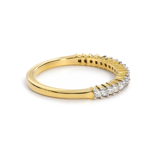 Close-up side angle of a yellow metal ring with a row of princess-shaped white gemstones in prong settings along the top half.