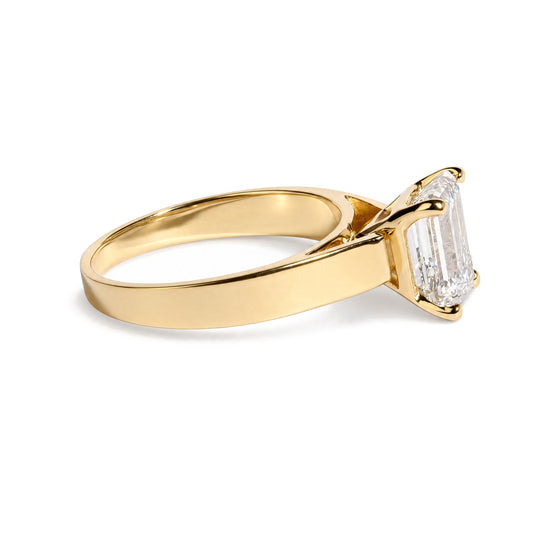 Close-up side angle of a yellow metal ring featuring a white gemstone in an emerald shape held by a four-prong setting.