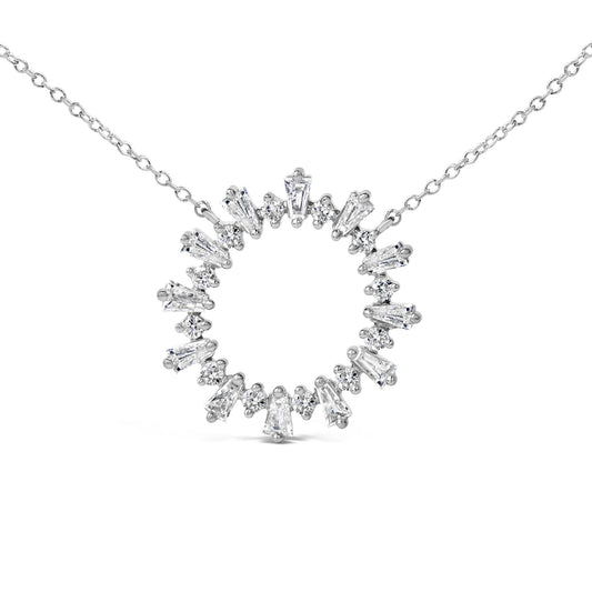 Close-up front angle of a white metal necklace pendant in a circular shape, set with alternating baguette and round white gemstones, shown on a white background.