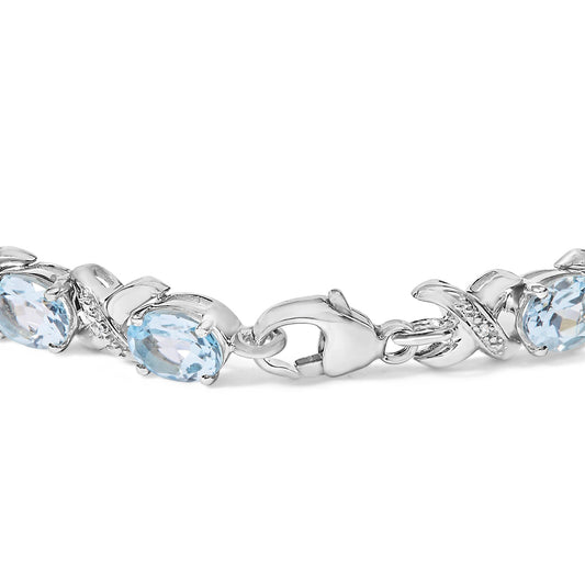 Close-up front angle of a white metal bracelet with blue oval gemstones in prong settings and small round white gemstones in prong settings intertwined near the clasp.