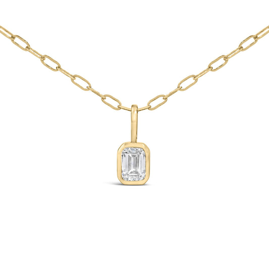 Close-up front angle of a yellow metal necklace with an emerald-shaped white gemstone in a bezel setting pendant.