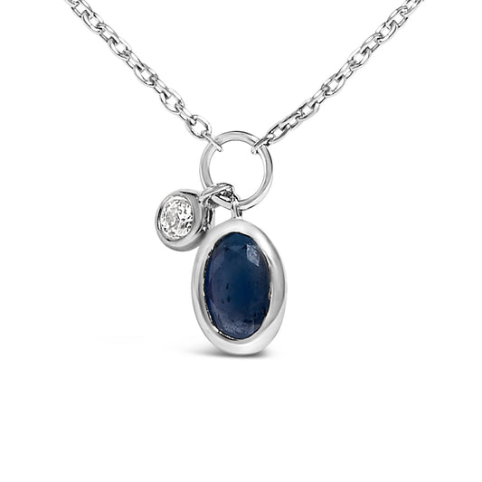 Close-up front angle of a white metal necklace with two bezel-set pendants: an oval blue gemstone and a smaller round white gemstone.