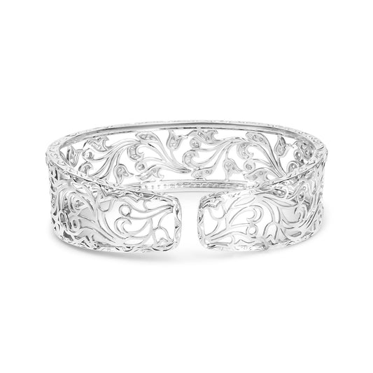 Front-facing shot of an open white metal cuff bracelet with intricate scrollwork and round white gemstones in a pave setting throughout the design.