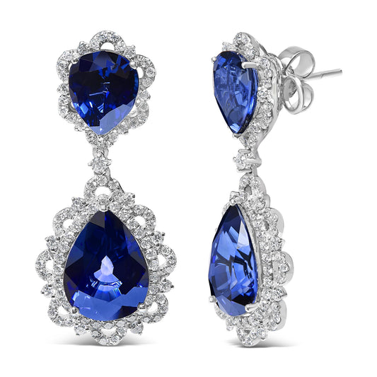 Pair of white metal drop earrings with pear-shaped blue gemstones surrounded by small white gemstones, shown from front and side angles.