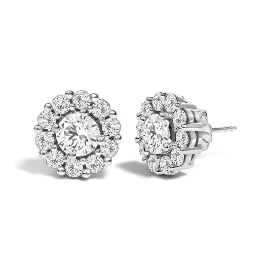 Pair of white metal stud earrings with a central round white gemstone in four-prong setting, surrounded by smaller round white gemstones in shared prong setting, shown from a front and side angle on a white background.
