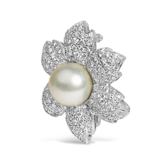 White flower-shaped brooch angled right, featuring pave-set round white gemstones on petals with a large central light-colored pearl-like gemstone.