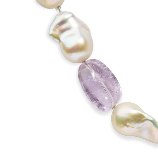 Close-up angled view of a yellow metal necklace featuring irregular-shaped white pearls and a translucent light purple gemstone with a drilled setting.