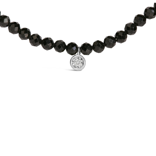 Close-up front view of a white metal necklace featuring round black faceted gemstones and a single round white gemstone pendant in miracle setting.