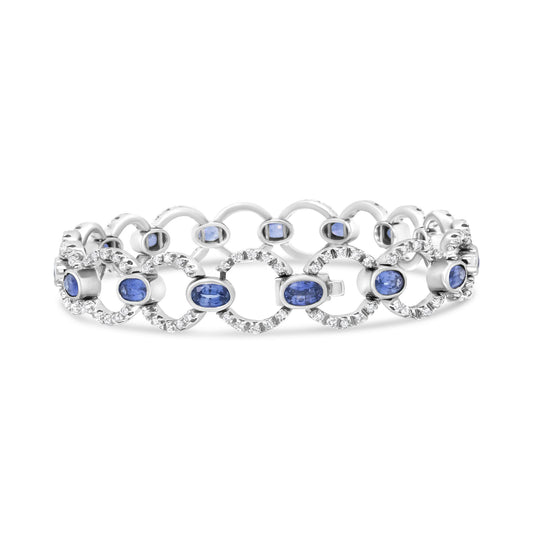 White metal bracelet with alternating open circular links adorned with round white gemstones and oval blue gemstones in bezel settings, shown from a front angle.