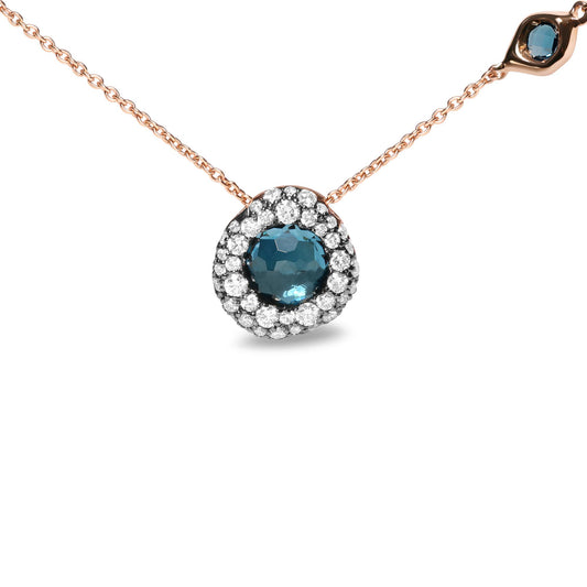 Close-up front angle of a rose metal necklace with a round blue gemstone pendant surrounded by small white gemstones in prong setting, featuring an additional small round blue gemstone and a small white gemstone in bezel settings on the chain.