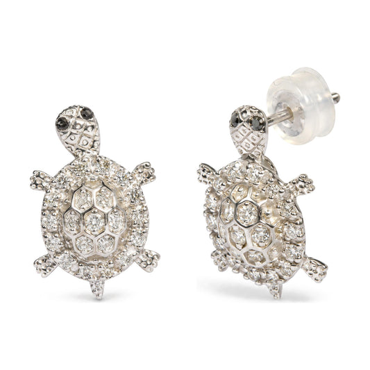 Close-up front angle of a pair of white metal turtle-shaped stud earrings with round white gemstones covering the body and black gemstones on the head, shown on a white background.