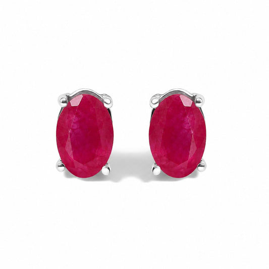 Close-up front angle of a pair of white metal stud earrings featuring oval-shaped red gemstones in four-prong settings shown on a white background.