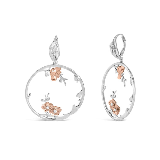 Front and side view of white and rose colored metal earrings with open circular design, floral accents, and small white gemstones, isolated on white background.