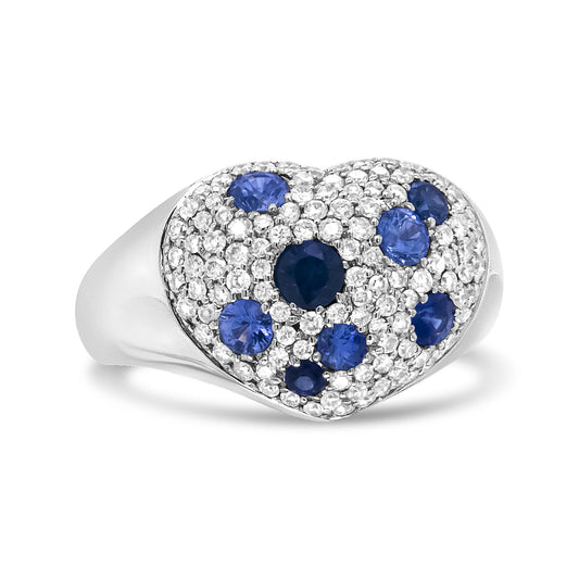 White metal heart-shaped ring with round white gemstones and scattered round blue gemstones in pave settings, shown at a slight side angle.