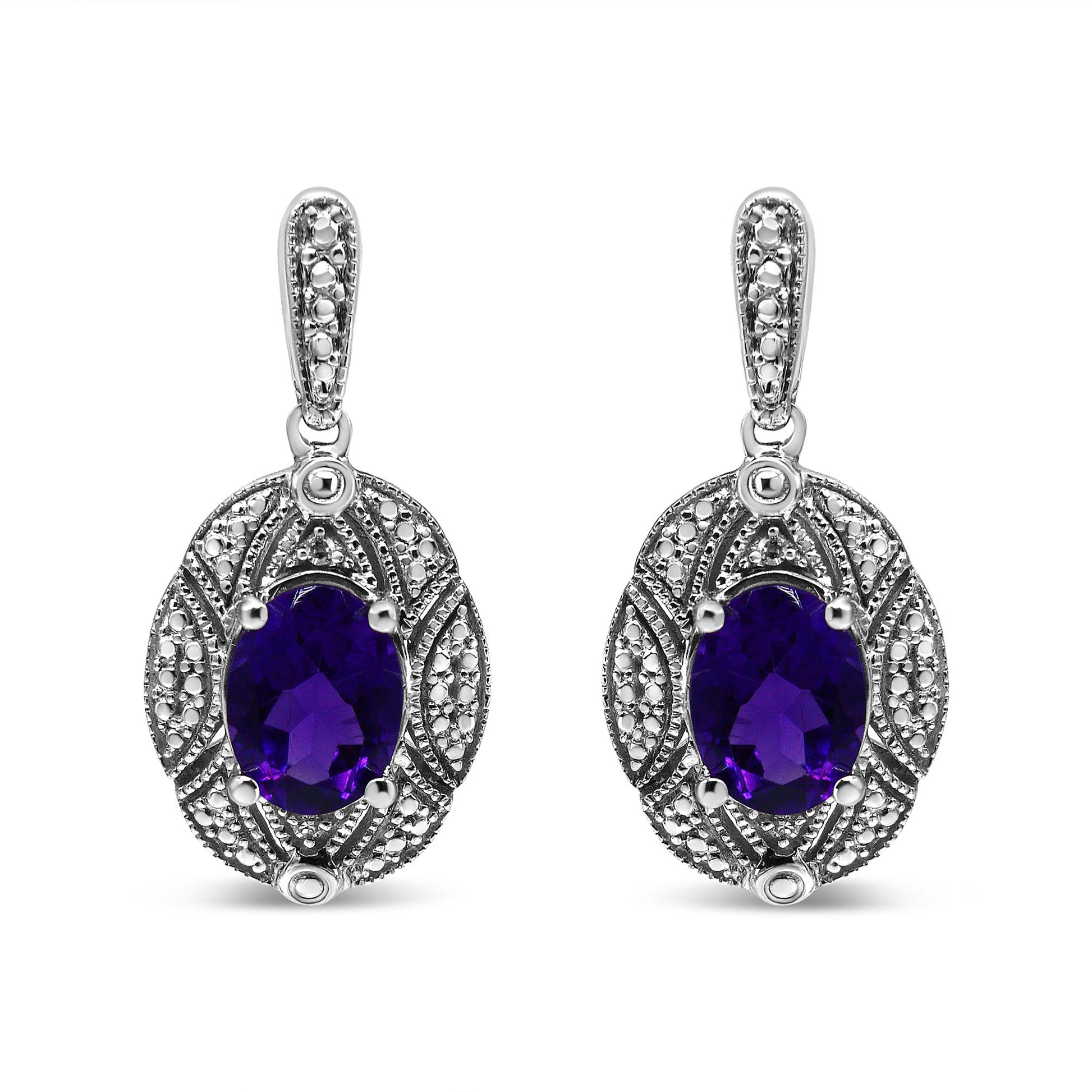 Front view of white metal drop earrings with oval purple gemstones surrounded by intricate detailing with small round white gemstones in prong settings.