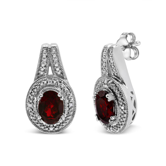 Pair of white metal earrings with oval red gemstones surrounded by small round white gemstones, shown from front and side angles.
