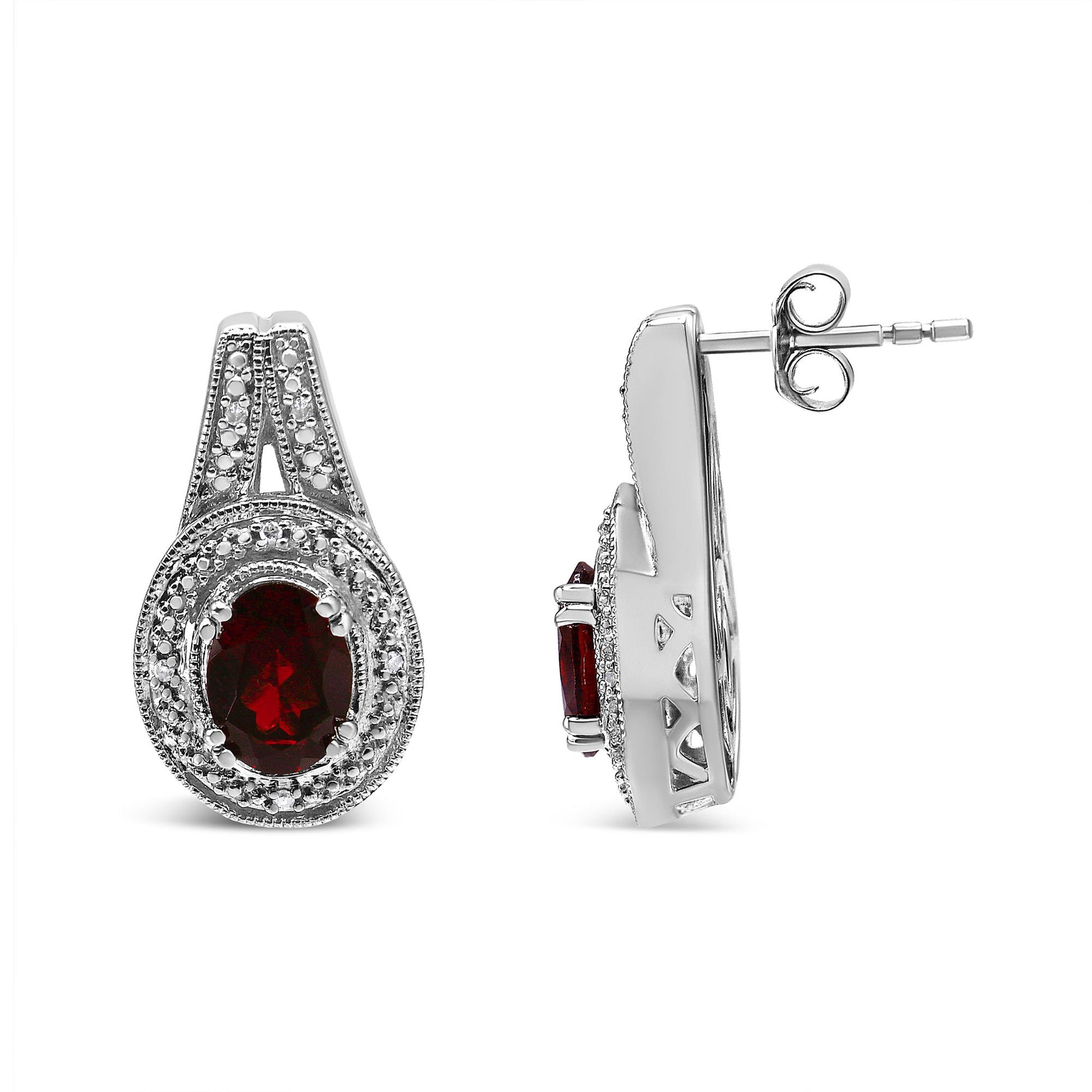Front and side views of white metal earrings with oval red gemstones surrounded by round white gemstones in prong settings.