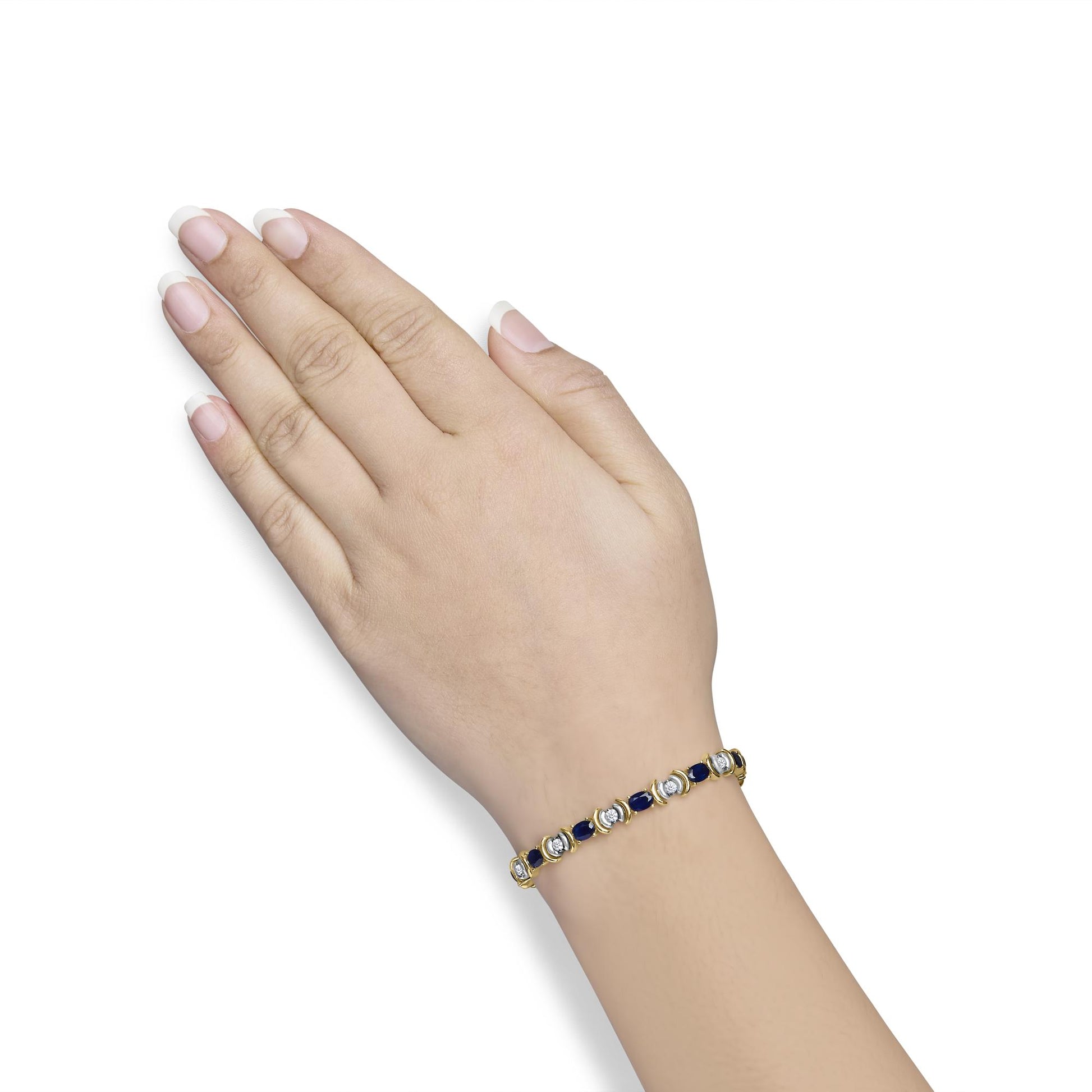 Yellow metal bracelet with alternating round white gemstones in two-prong settings and oval blue gemstones in four-prong settings, shown worn on a model's wrist from a top angle.