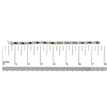Top-down view of a yellow metal bracelet with alternating blue oval gemstones and white round gemstones, shown on a ruler for size reference.