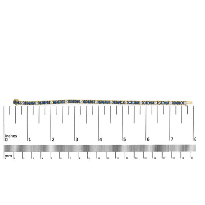 Yellow metal bracelet with alternating round blue and white gemstones in 4-prong settings, laid flat on a ruler for size reference, top-down view.