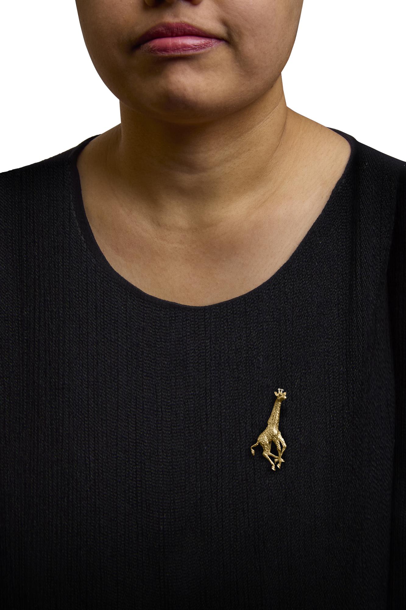 Brooch shaped like a giraffe in yellow metal with white and blue round gemstones, shown worn on a model's black top, front view.