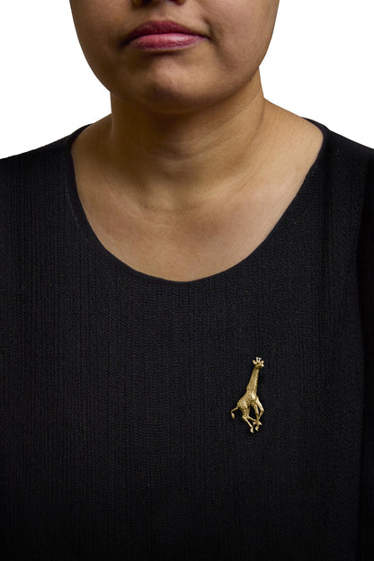 Brooch shaped like a giraffe in yellow metal with white and blue round gemstones, shown worn on a model's black top, front view.