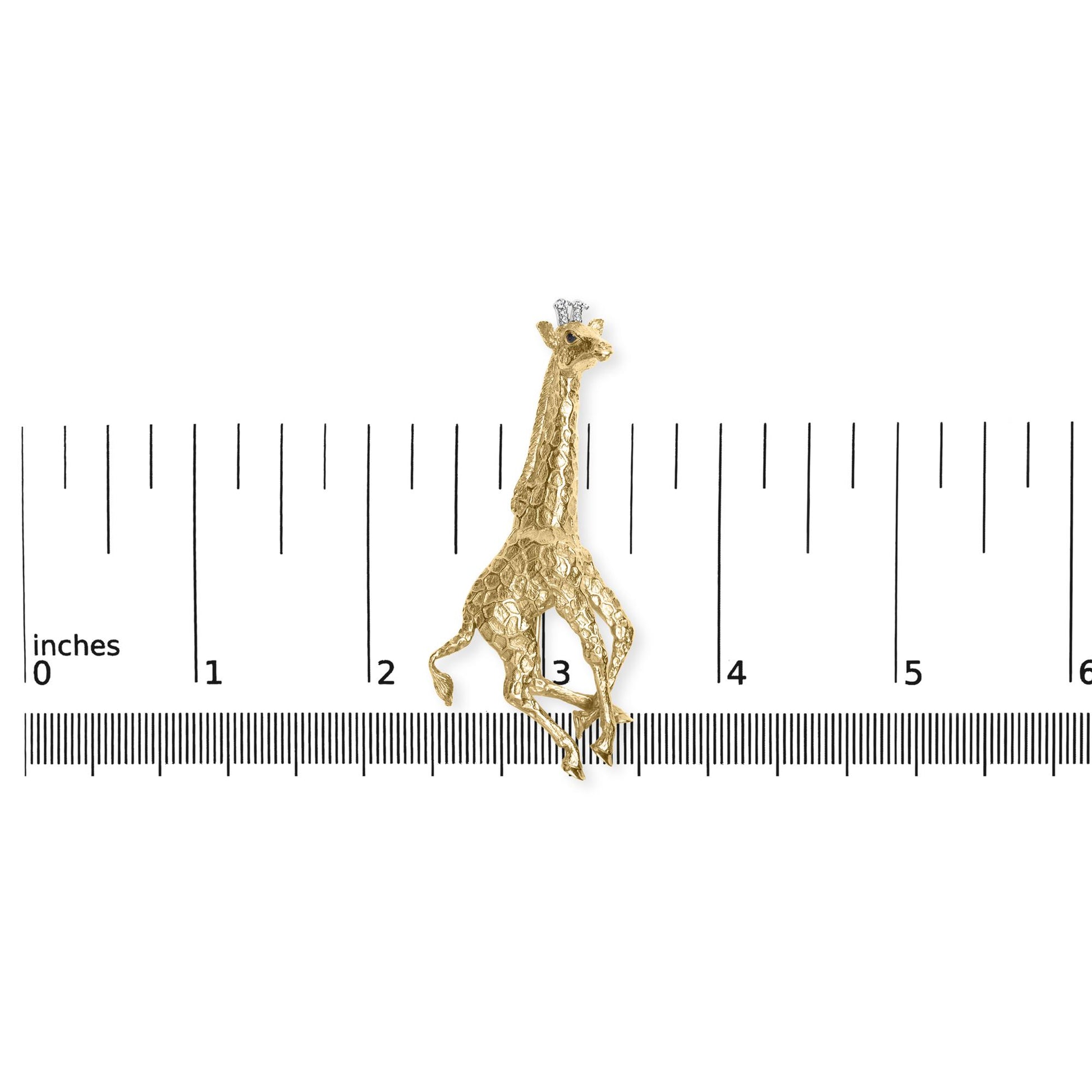 Close-up front angle of a yellow giraffe-shaped brooch with textured detail, adorned with round white gemstones in a shared prong setting on the giraffe's head, and round blue gemstones in bezel settings on the crown and eyes, placed on a ruler for size reference.