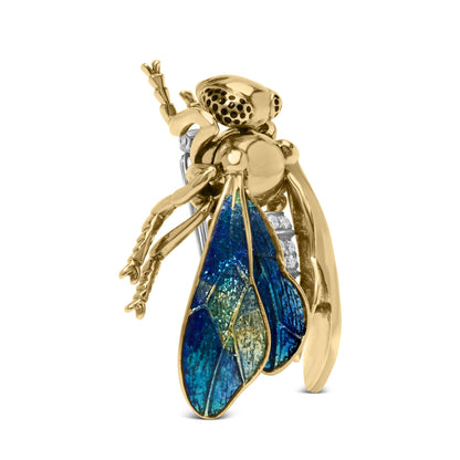 Close-up side view of a yellow metal insect-shaped brooch with iridescent blue wings and small white gemstones on its back.