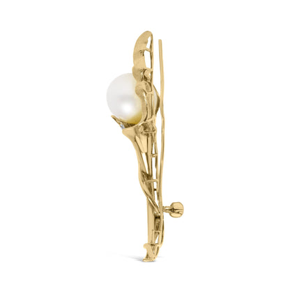 Side view of a yellow metal brooch with a large white pearl and small white gemstones in pave setting.