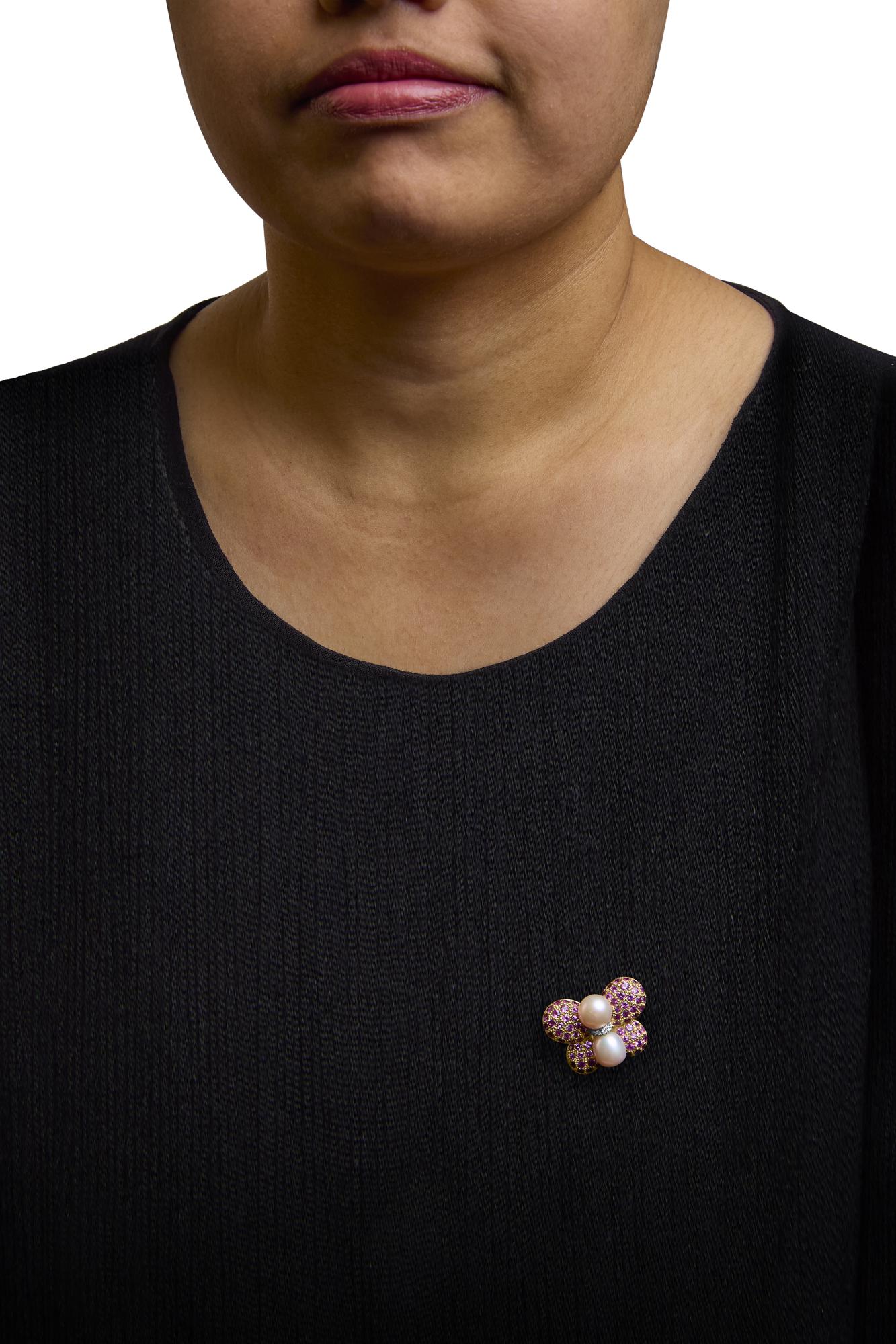 Brooch with yellow and white metal, featuring clusters of round pink gemstones and two white pearls, shown worn on a model's black top, front-facing angle.