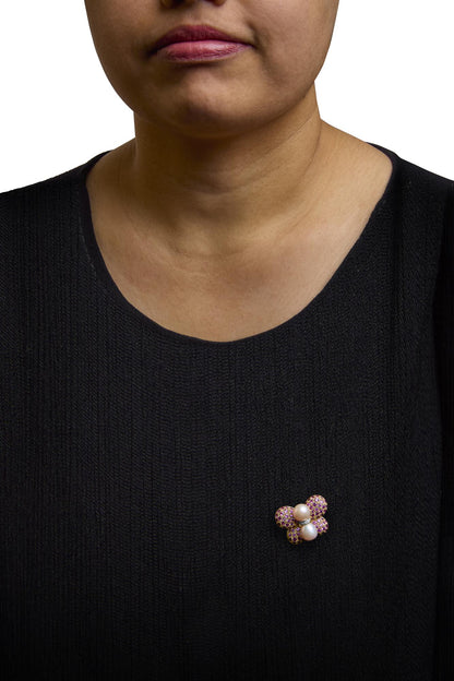 Brooch with yellow and white metal, featuring clusters of round pink gemstones and two white pearls, shown worn on a model's black top, front-facing angle.