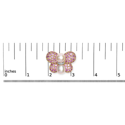 Brooch shaped like a butterfly with pink gemstones and white gemstones on yellow and white metal, photographed from above on a ruler for size reference.