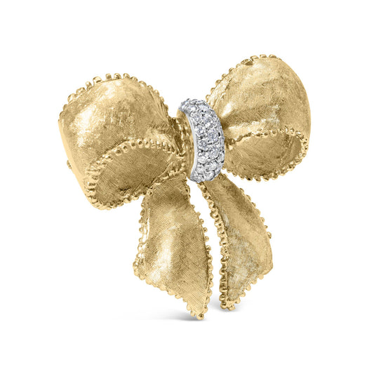 Front angled view of a yellow metal bow-shaped brooch with textured surface and beaded edges, featuring a cluster of round white gemstones in shared prong setting at the center.