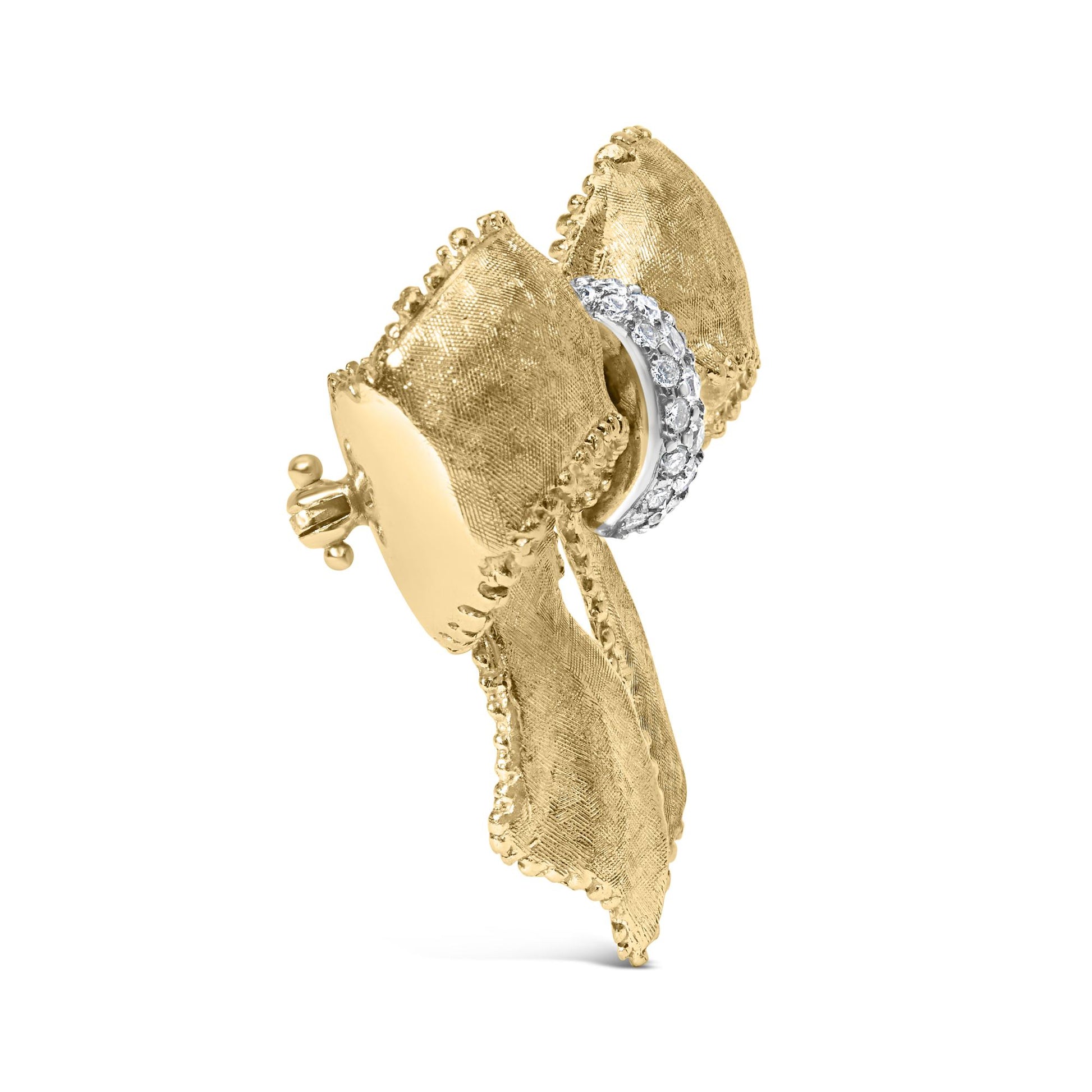 Side angle view of a yellow metal bow-shaped brooch with textured edges and a curved section set with round white gemstones in shared prong setting.