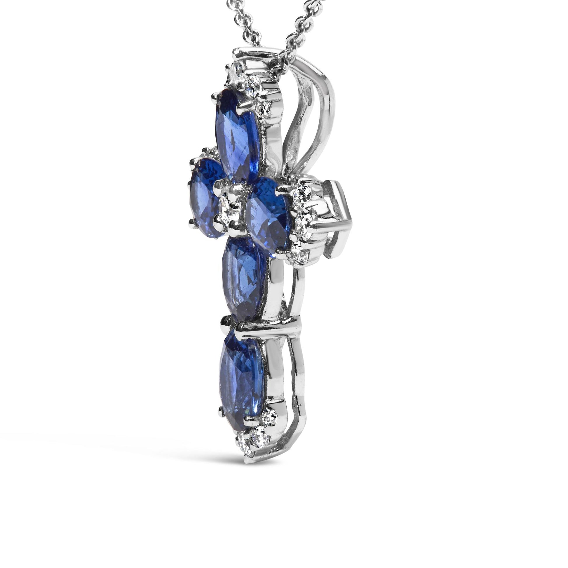 Close-up side-angle view of a white necklace pendant in a cross shape with oval blue gemstones and round white gemstones in shared prong settings, shown on a white background.