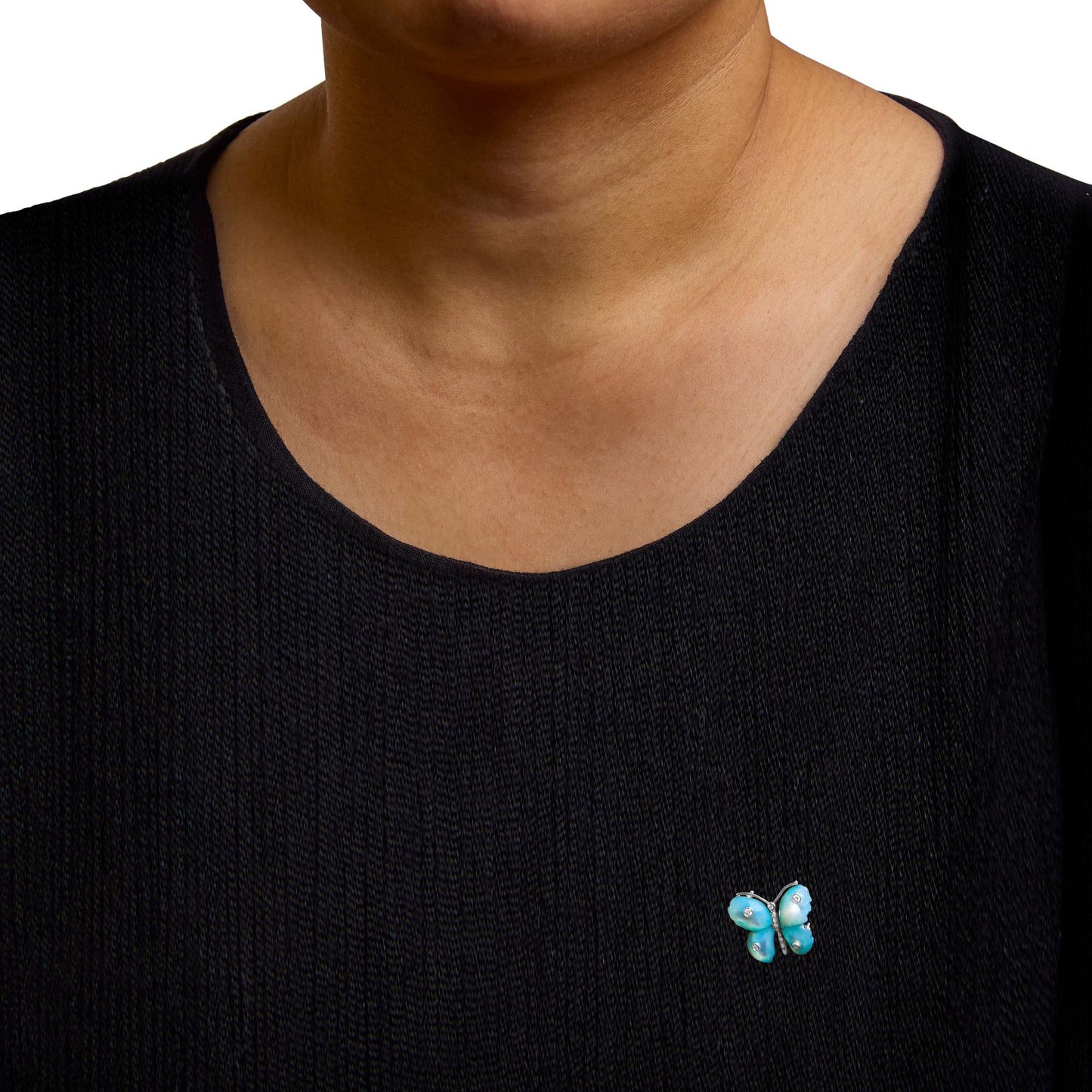 White metal butterfly-shaped brooch with blue wings accented by white round gemstones in bezel and pave settings, worn on a model's black top, shown from the front.