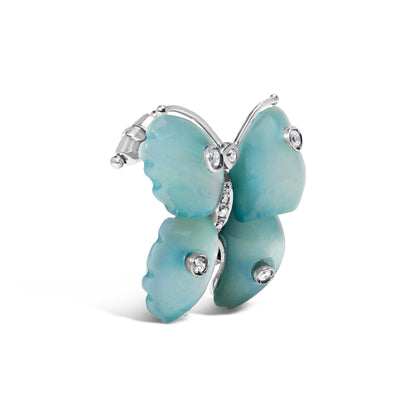 White metal butterfly-shaped brooch with blue wings featuring round bezel and pave-set white gemstones, shown at a side angle on a white background.