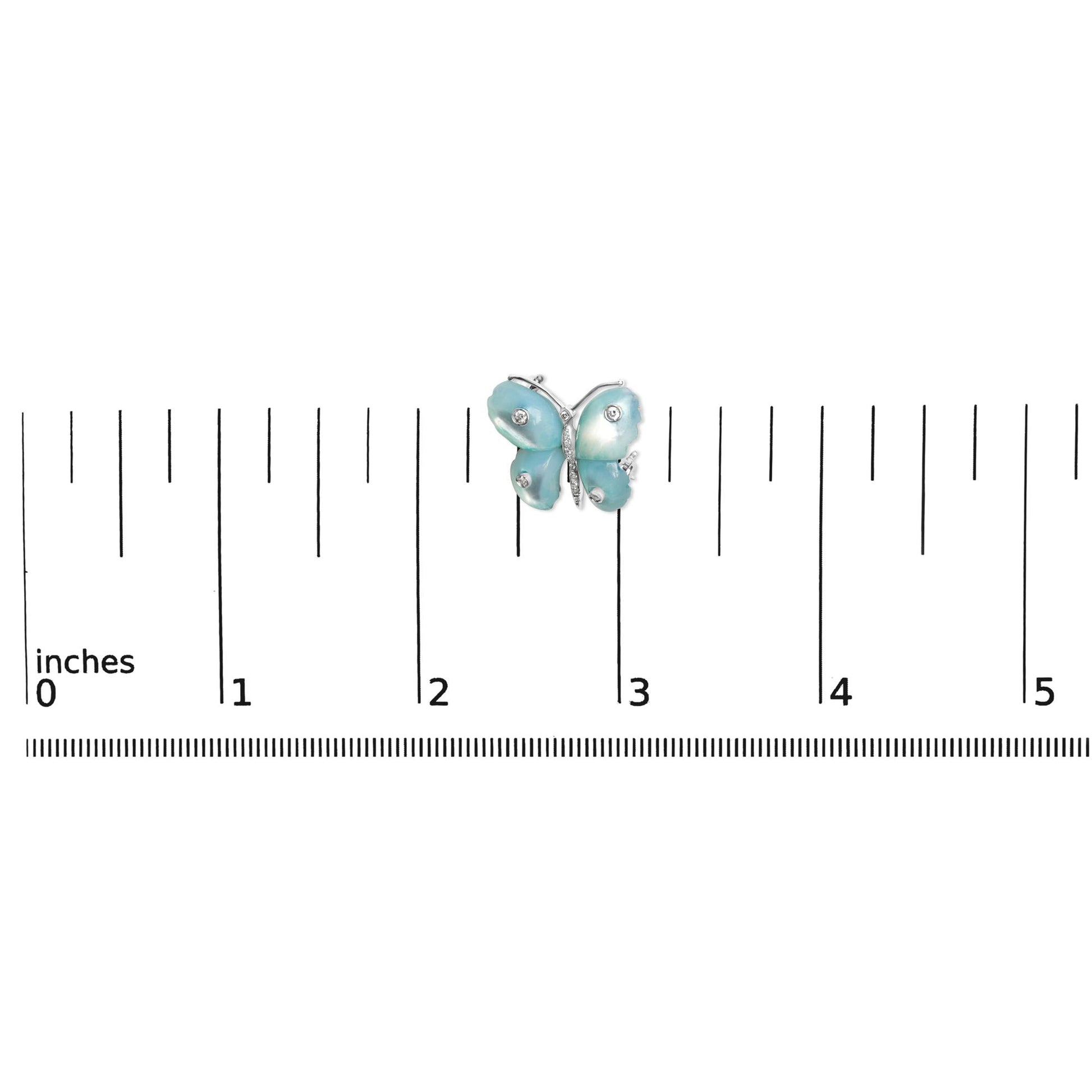 White metal butterfly-shaped brooch with blue wings accented by round white gemstones in bezel and pave settings, shown on a scale from a top-down angle.