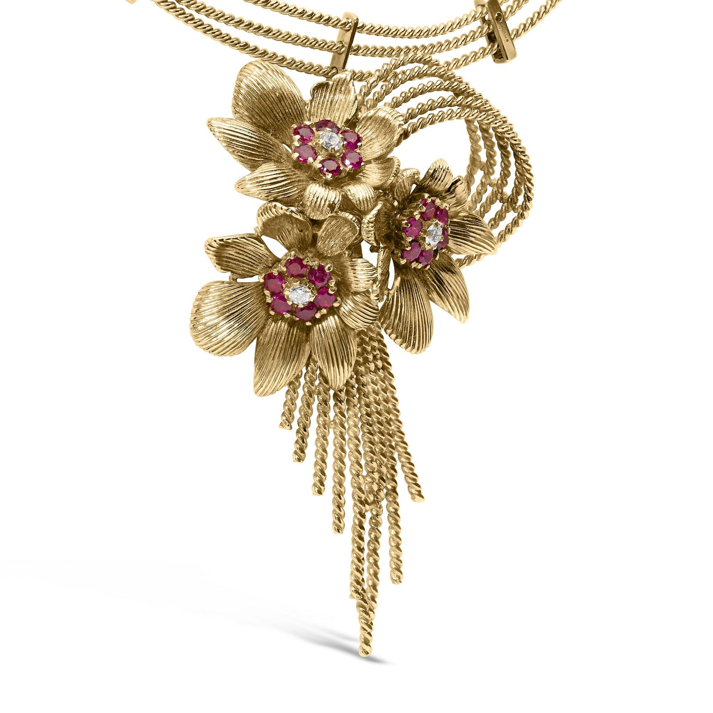 Close-up front angle of a yellow metal necklace with three textured flower pendants, each featuring a cluster of red and white round gemstones in the center, and multiple twisted chain tassels hanging below.