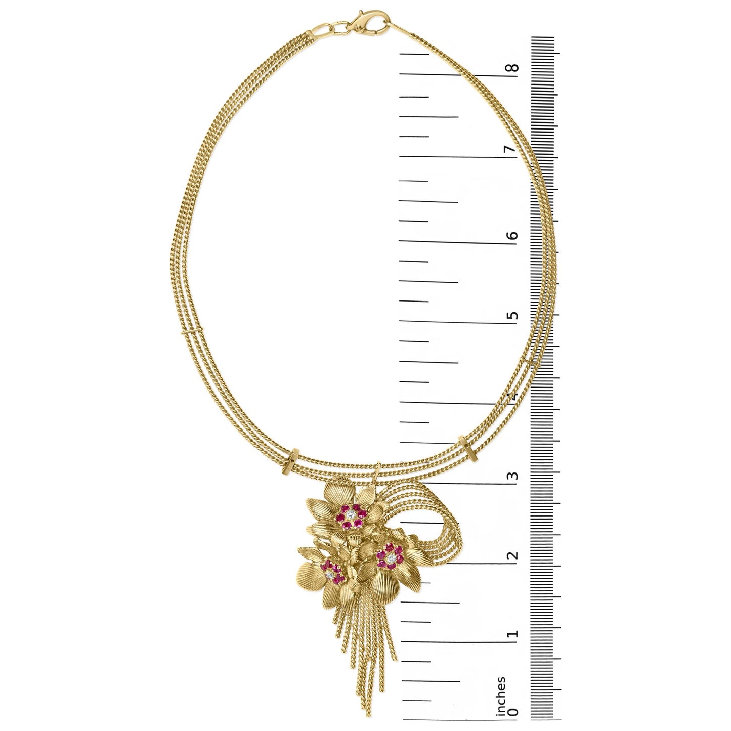 Top-down view of a yellow metal necklace with a floral pendant set with white and red gemstones, shown on a ruler for size reference.