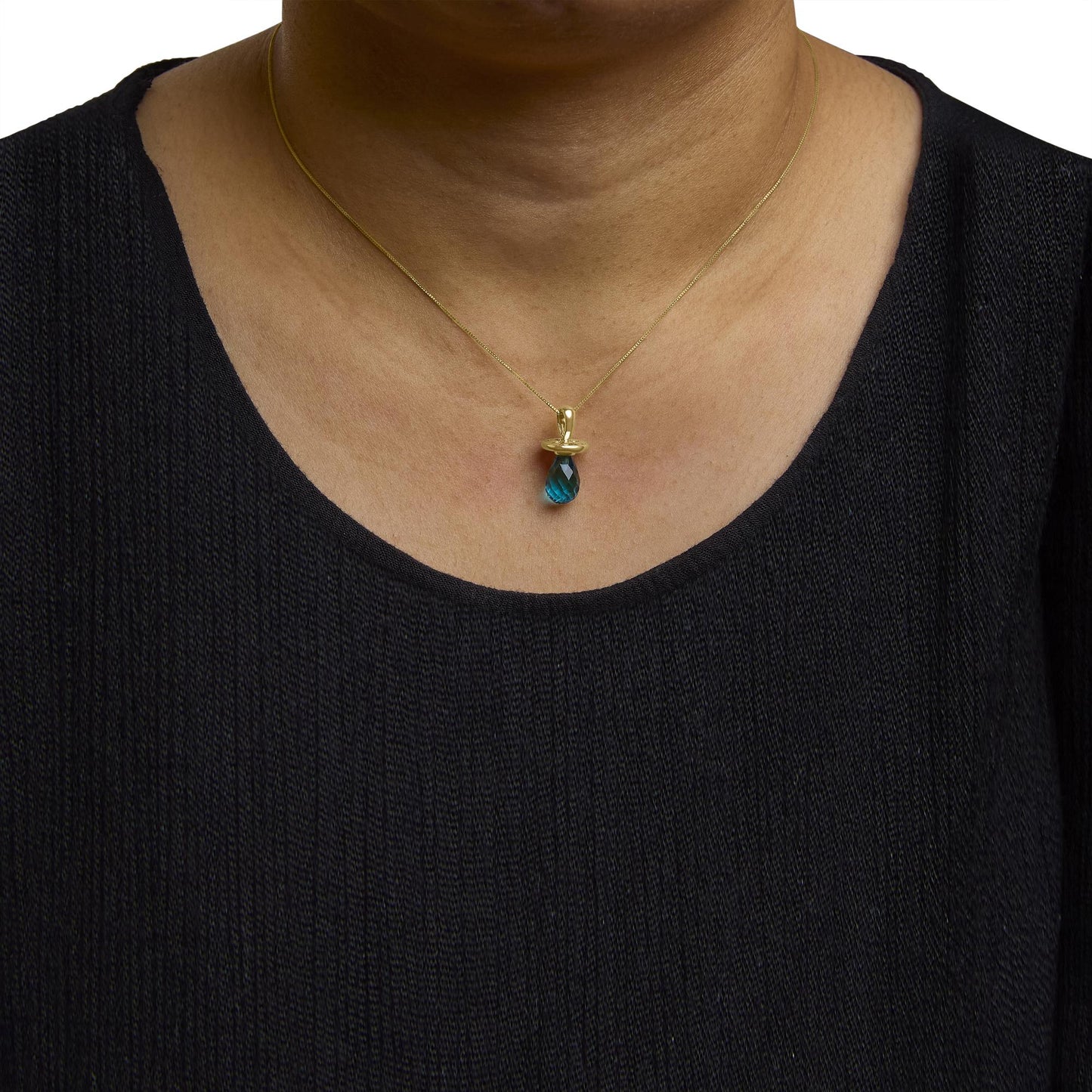 Close-up front view of a model wearing a yellow metal necklace with a small blue gemstone pendant in a drilled setting.