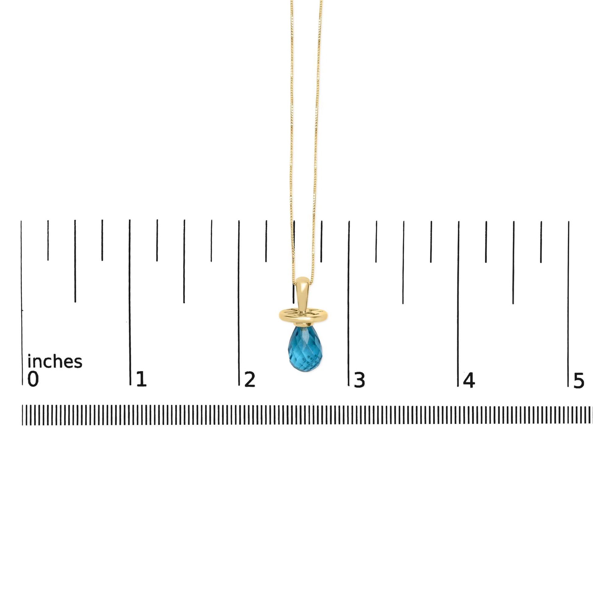 Yellow metal necklace with a blue faceted teardrop-shaped gemstone pendant, shown hanging against a ruler scale from a front angle.