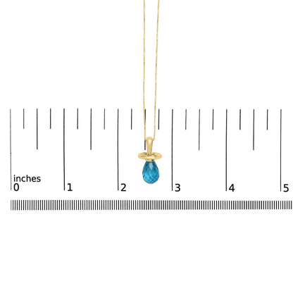Yellow metal necklace with a blue faceted teardrop-shaped gemstone pendant, shown hanging against a ruler scale from a front angle.