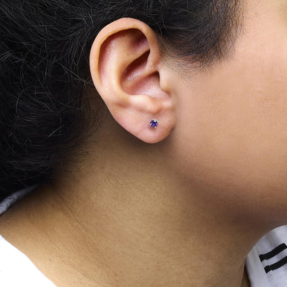 Close-up side view of a white metal stud earring with a round purple gemstone in a 4-prong setting, worn on a model's ear.