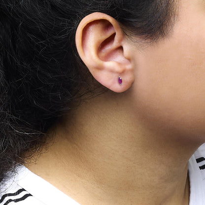 Close-up side view of a white metal earring with a marquise-shaped pink gemstone in a two-prong setting, worn on a model's ear.