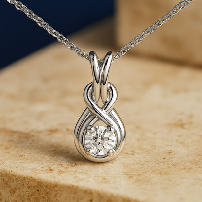 Close-up front view of a white metal necklace with an infinity-shaped pendant holding a single round white gemstone in a prong setting, shown on a beige surface.