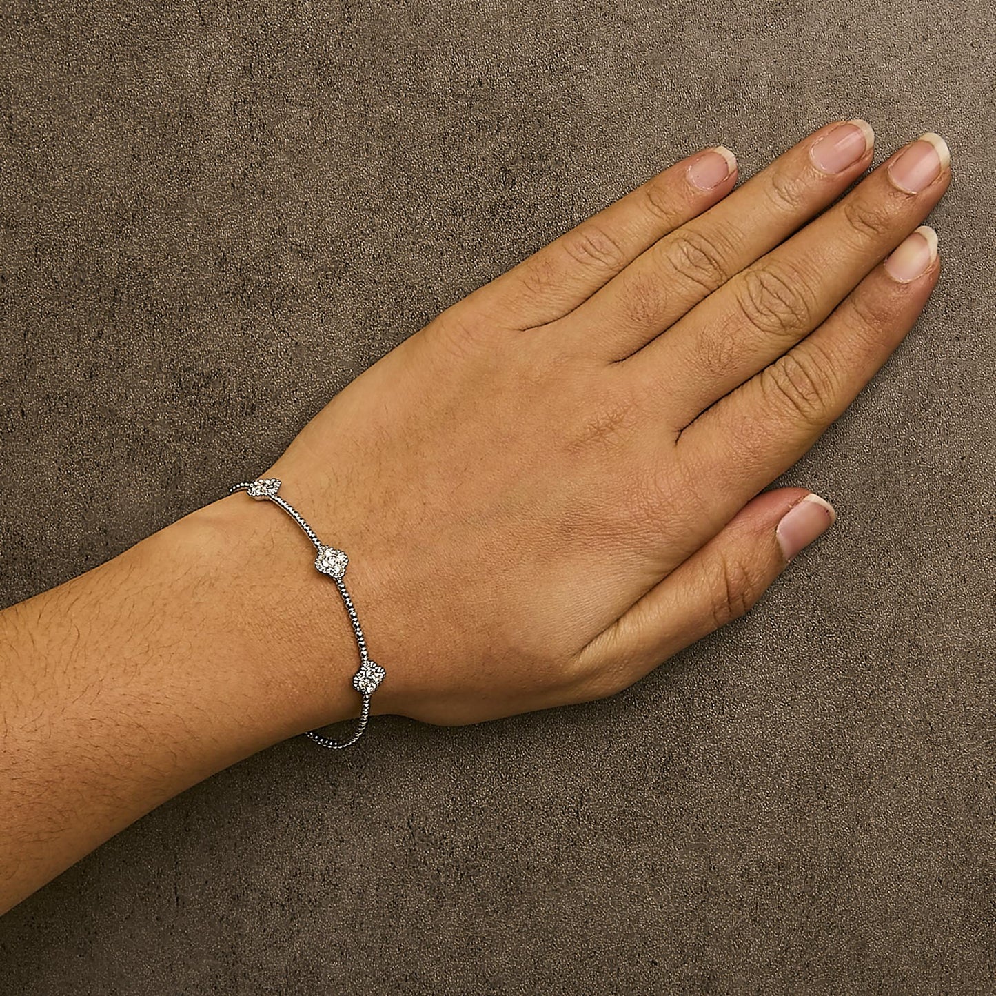 White metal bracelet with round white gemstones in shared prong settings, shown worn on a model's wrist in a top-down angle.