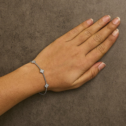 White metal bracelet with round white gemstones in shared prong settings, shown worn on a model's wrist in a top-down angle.